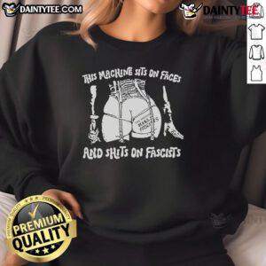 Alt Text: Hot This Machine Sits On Faces and Shits On Fascists sweatshirt displayed on a hanger, featuring bold graphic design.