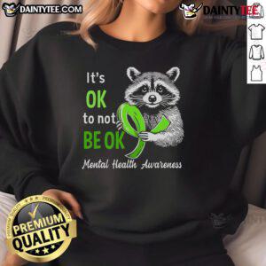 Funny raccoon graphic on a sweatshirt with the phrase It's okay to not be okay, promoting mental health awareness.