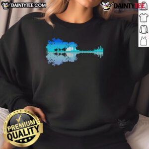 Musician wearing a 'Good Guitar' sweatshirt by the lake, capturing the essence of music and nature in a serene setting.