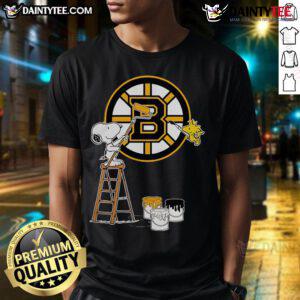 Snoopy and Woodstock painting Boston Bruins logo on a t-shirt, showcasing a fun and vibrant sports design.