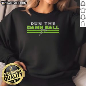 Alt Text: Kenneth Walker III wearing a Seattle Seahawks signature sweatshirt with Hot Run the Damn Ball slogan.